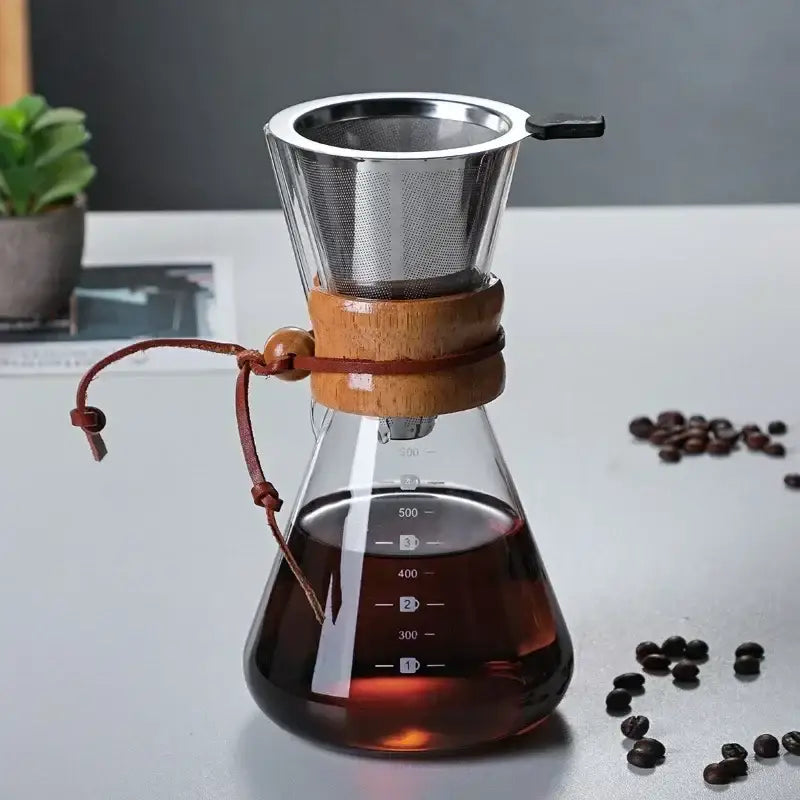 A clear glass coffee kettle with wooden collar and steel filter drip featuring a brown leather tie for brewing
