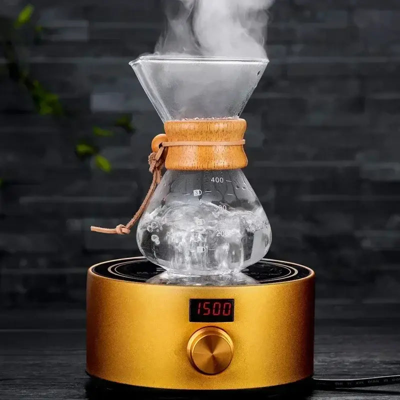 A clear glass coffee kettle with wooden collar and steel filter drip brews on a golden electric filter drip brewer base