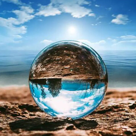 A clear transparent glass crystal ball resting on sandy ground modern glass crystal decor photography prop