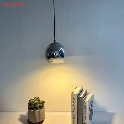 A sleek spherical chrome glass pendant light with reflective surface hanging from a black cord for an inviting atmosphere