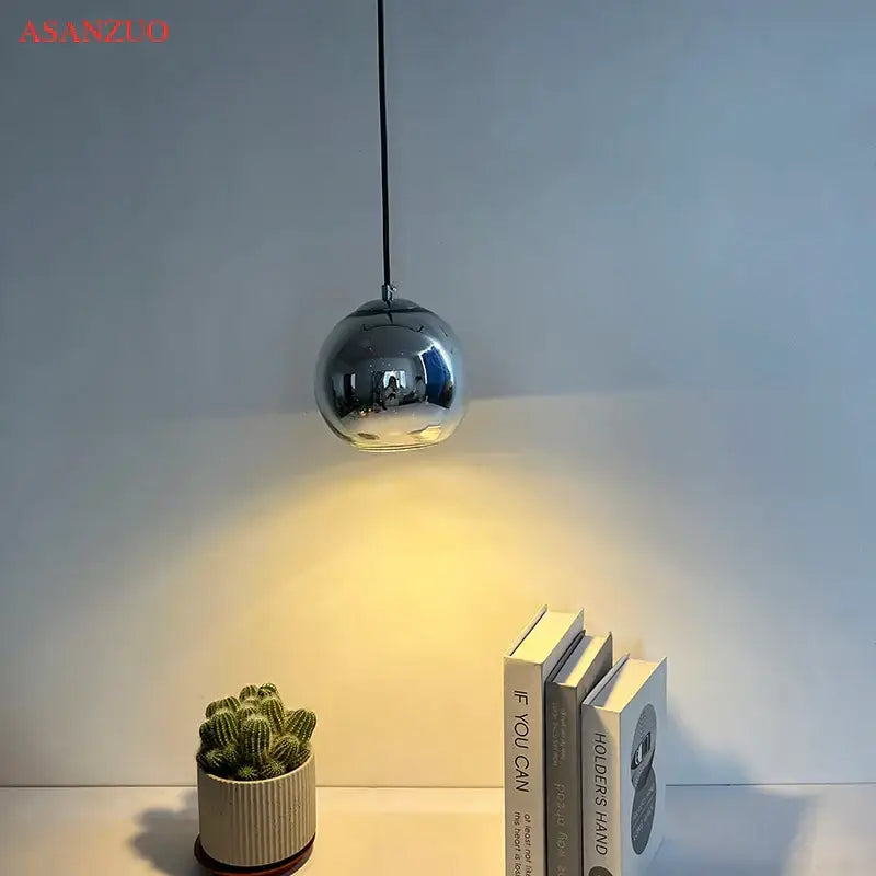 A sleek spherical chrome glass pendant light with reflective surface hanging from a black cord for an inviting atmosphere