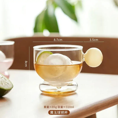 Clear glass coffee mug with a rounded translucent yellow glass spherical handle and a footed base for kitchen use