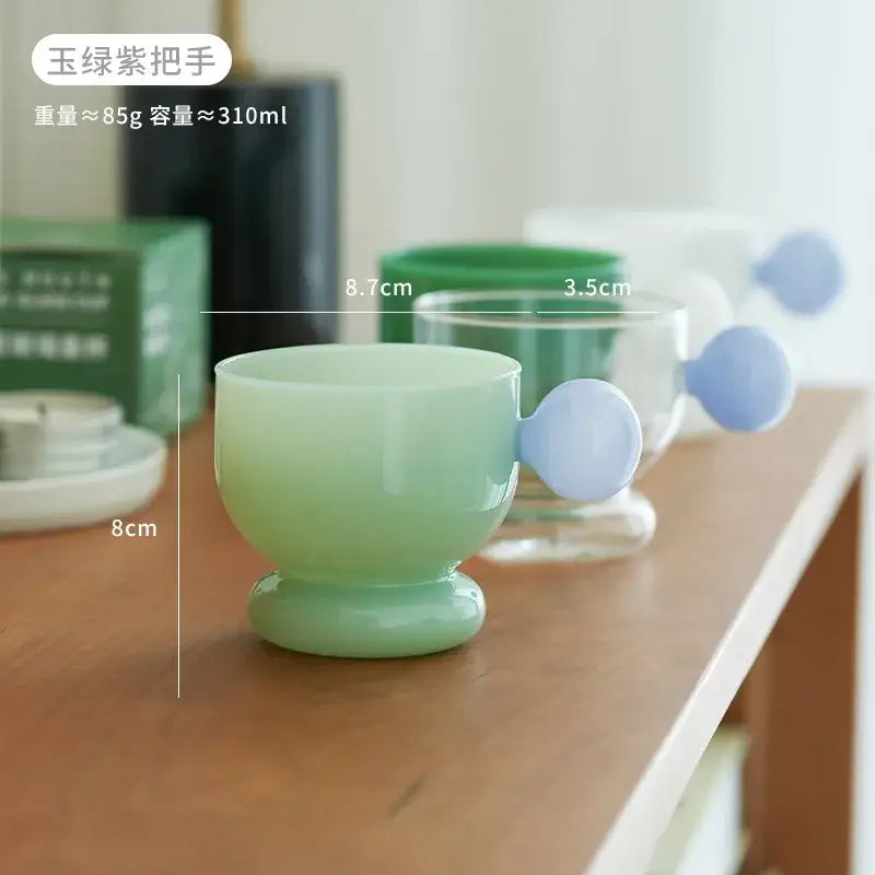 Modern glass spherical handle coffee mug in translucent jade green with a rounded lavender spherical handle