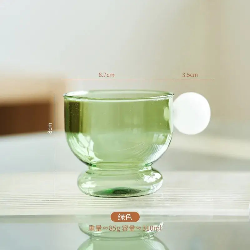 Translucent green glass coffee mug with a spherical handle and sturdy base ideal for modern kitchen decor