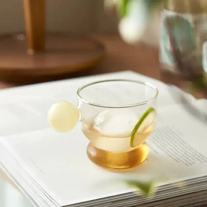 Modern glass coffee mug with a spherical handle and bulbous base filled with amber liquid and lime garnish