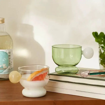 Modern translucent green glass coffee mug with a rounded white glass spherical handle and matching footed base