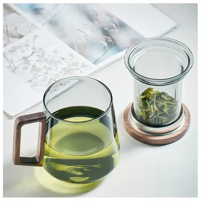 Modern glass tea cup with wood handle filled with green tea and matching infuser on wood and metal coaster decorbites glass tea