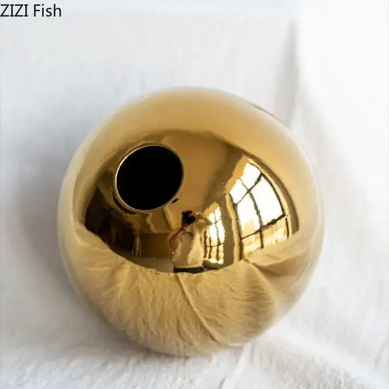 Shiny gold ceramic vase with smooth reflective surface and circular opening for modern decorbites golden ball decor