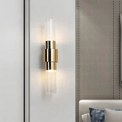Modern gold two light sconce with clear ribbed glass cylindrical accents and bulb base for bathroom use