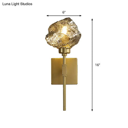 Modern gold wall sconce with textured amber smoke gray glass shade shaped like an irregular rock for living room use