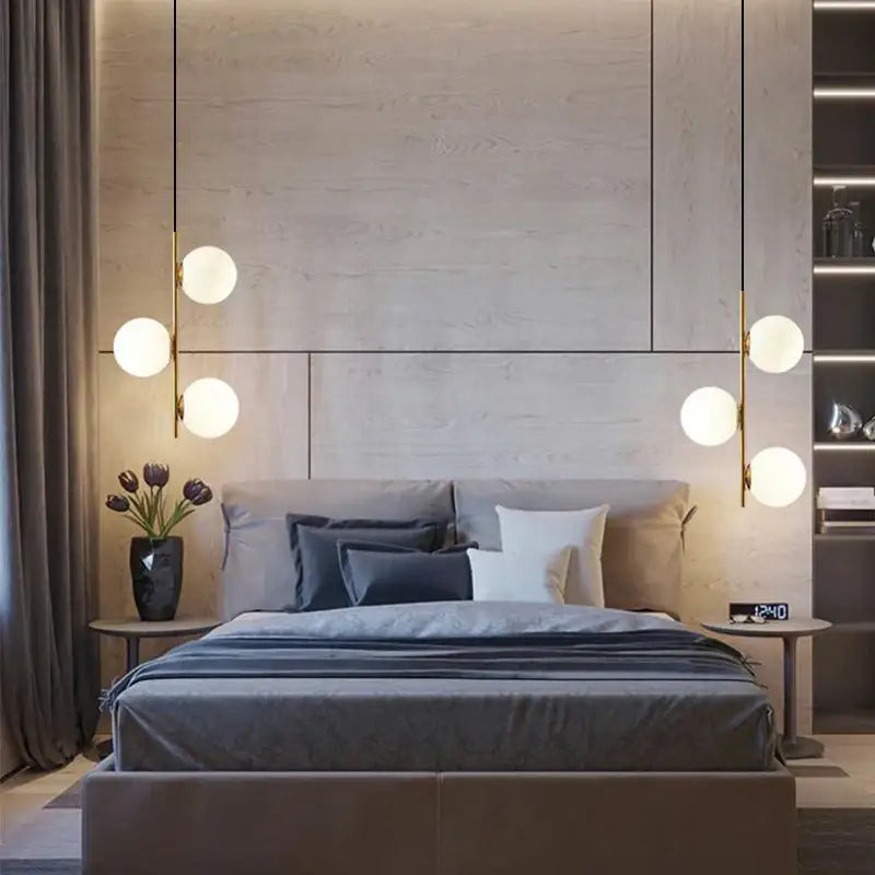 Modern gold and black glass ball led pendant lights hang in a minimalist bedroom with a gray upholstered bed