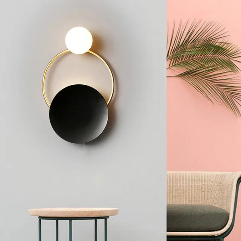 Modern gold and black orb wall lamp featuring a minimalist gold frame and illuminated white orb for living rooms