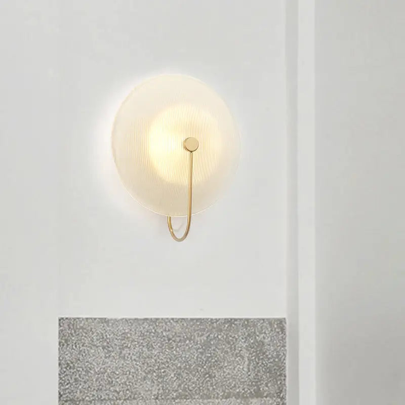 Minimalist wall lamp with a frosted circular glass shade and slender brass hardware for modern living rooms