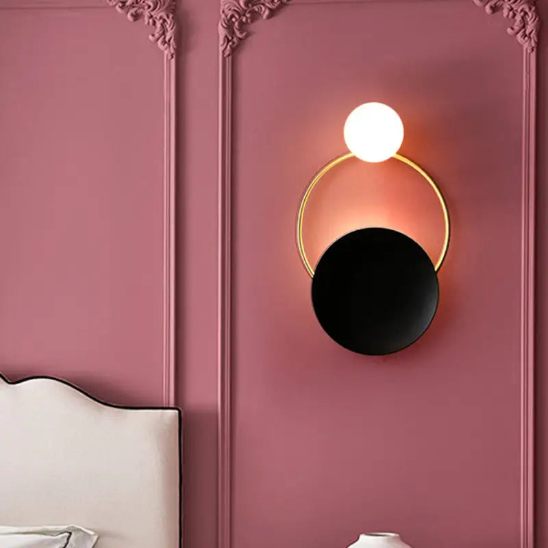 Modern gold and black orb wall lamp featuring a gold-toned circular frame and glowing white spherical bulb for living rooms