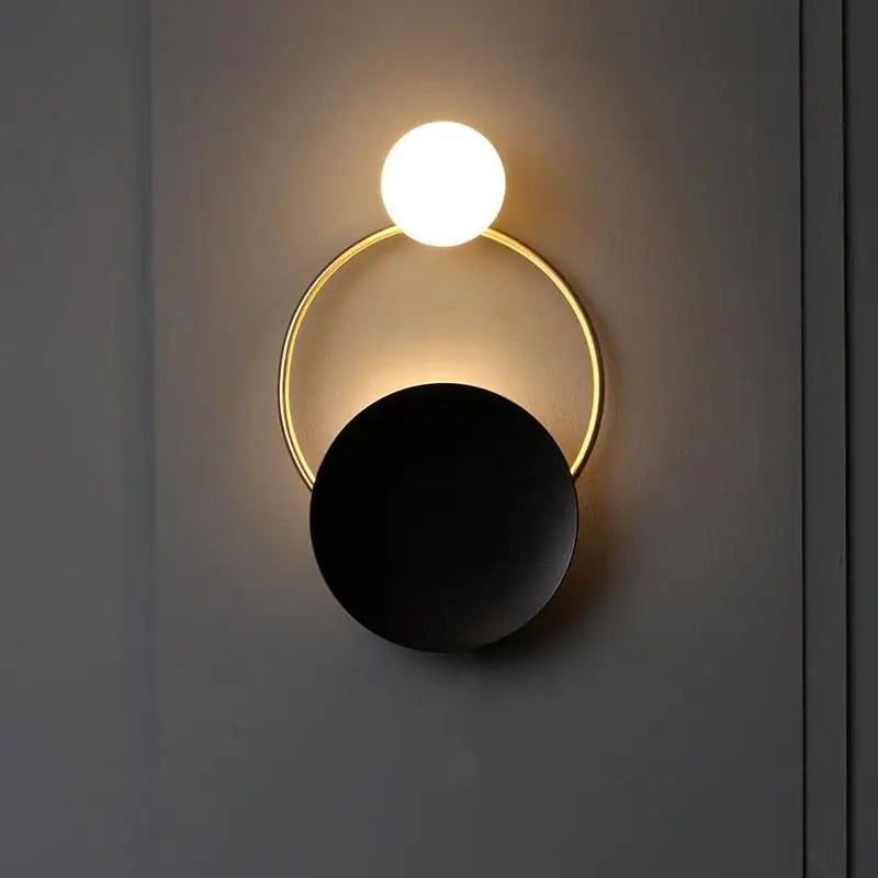 Modern gold and black orb wall lamp with a glowing white spherical bulb above a gold ring and matte black disc for living rooms