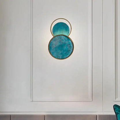 Modern teal circular wall lamp with brushed gold frame and textured glass panels for elegant living room decor