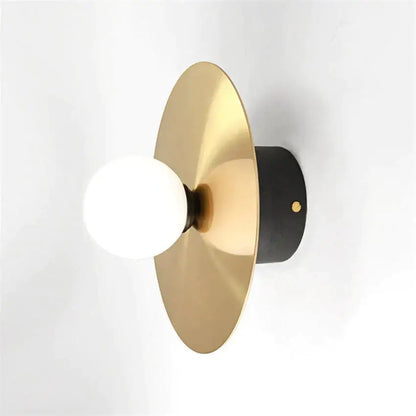 Modern gold and black riya wall light featuring a gold-toned disc sconce with matte black base and frosted glass bulb