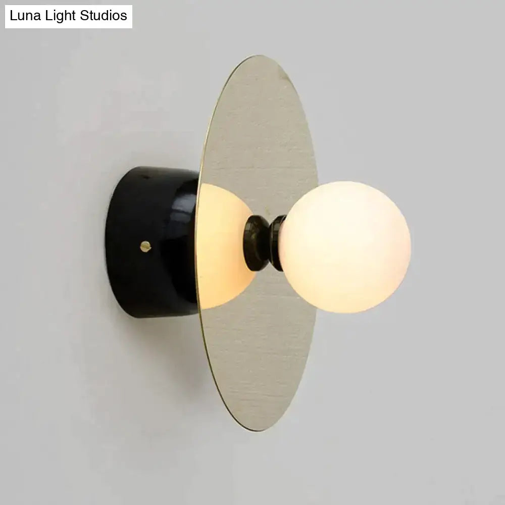 Modern gold and black riya wall light with black cylindrical base, brushed metal disc, and frosted glass globe bulbs