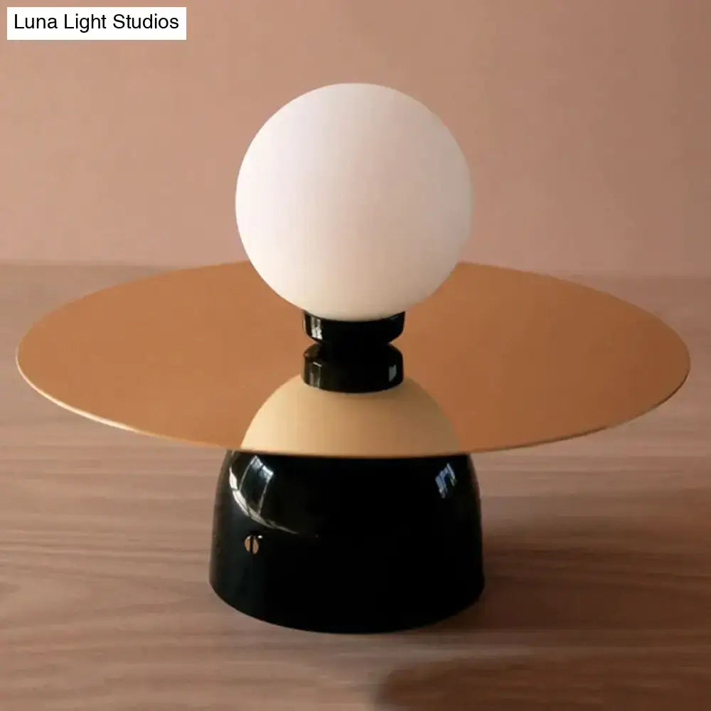 A modern gold and black riya wall light featuring a frosted glass spherical bulb on a circular metal base
