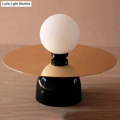 A modern gold and black riya wall light featuring a frosted glass spherical bulb on a circular metal base