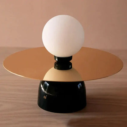 A modern riya wall light with a frosted glass spherical bulb, gold-toned platform, and glossy black base