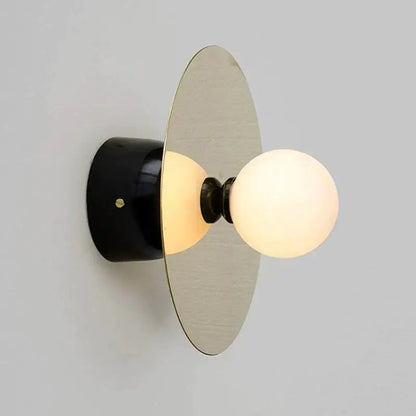 Modern gold and black riya wall light with sleek black cylindrical base, brushed metallic disc, and frosted glass bulbs