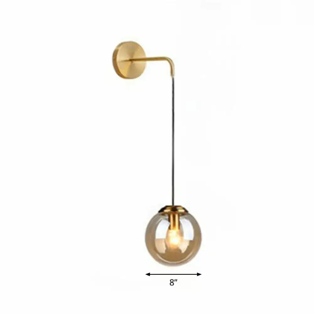 Modern gold and black spherical glass wall light with curved arm featuring an illuminated light bulb for living room use