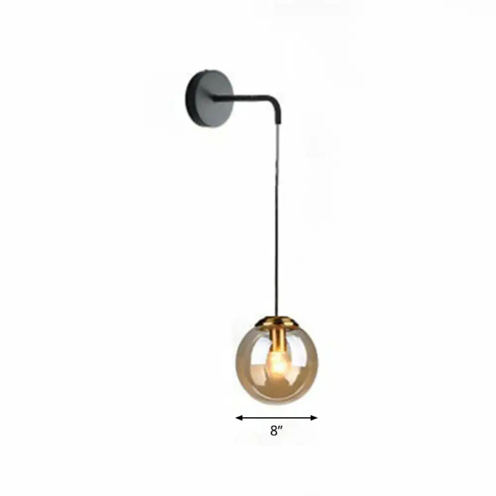 Modern gold and black spherical glass wall light featuring a black sconce with amber glass globe and brass-toned metal accents