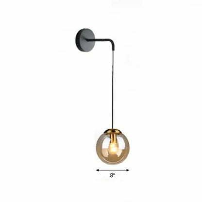Modern gold and black spherical glass wall light featuring a black sconce with amber glass globe and brass-toned metal accents