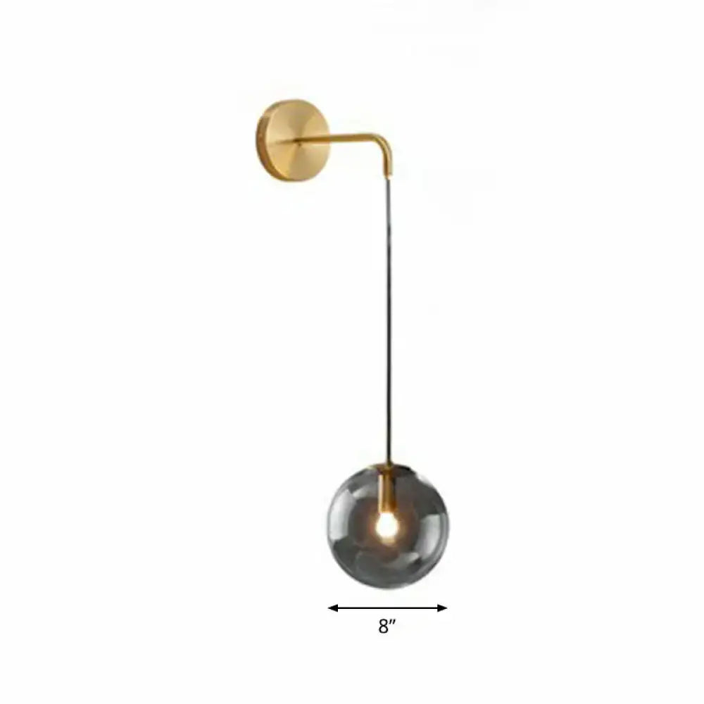 Modern gold and black spherical glass wall light with a gold metal arm and smoked glass globe housing illuminated bulb