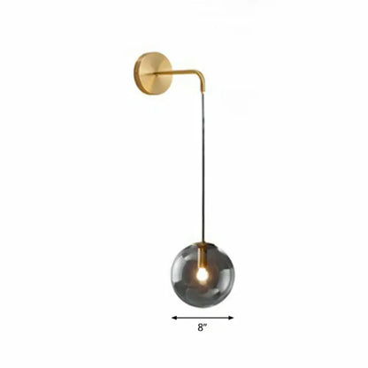 Modern gold and black spherical glass wall light with a gold metal arm and smoked glass globe housing illuminated bulb