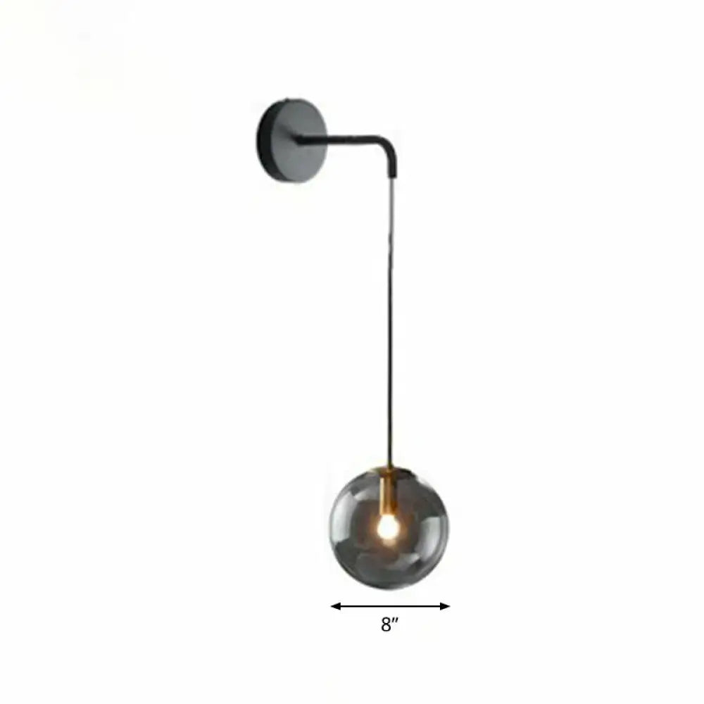Modern gold and black spherical glass wall light with a sleek curved arm and smoked glass light bulb for living room use