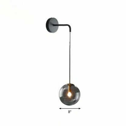 Modern gold and black spherical glass wall light with a sleek curved arm and smoked glass light bulb for living room use