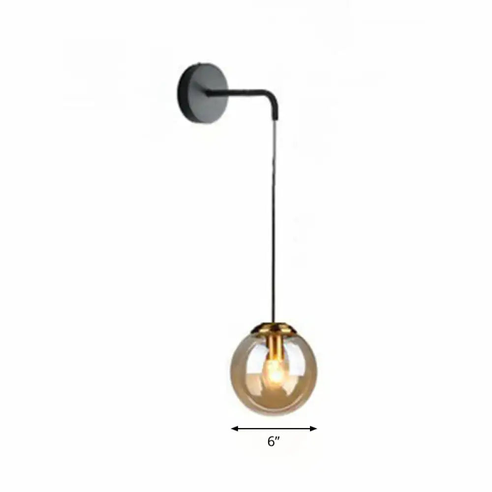 Modern gold and black spherical glass wall light with amber globe housing an illuminated light bulb for living room use