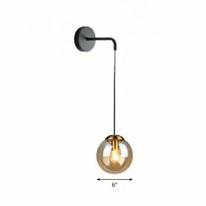 Modern gold and black spherical glass wall light with amber globe housing an illuminated light bulb for living room use
