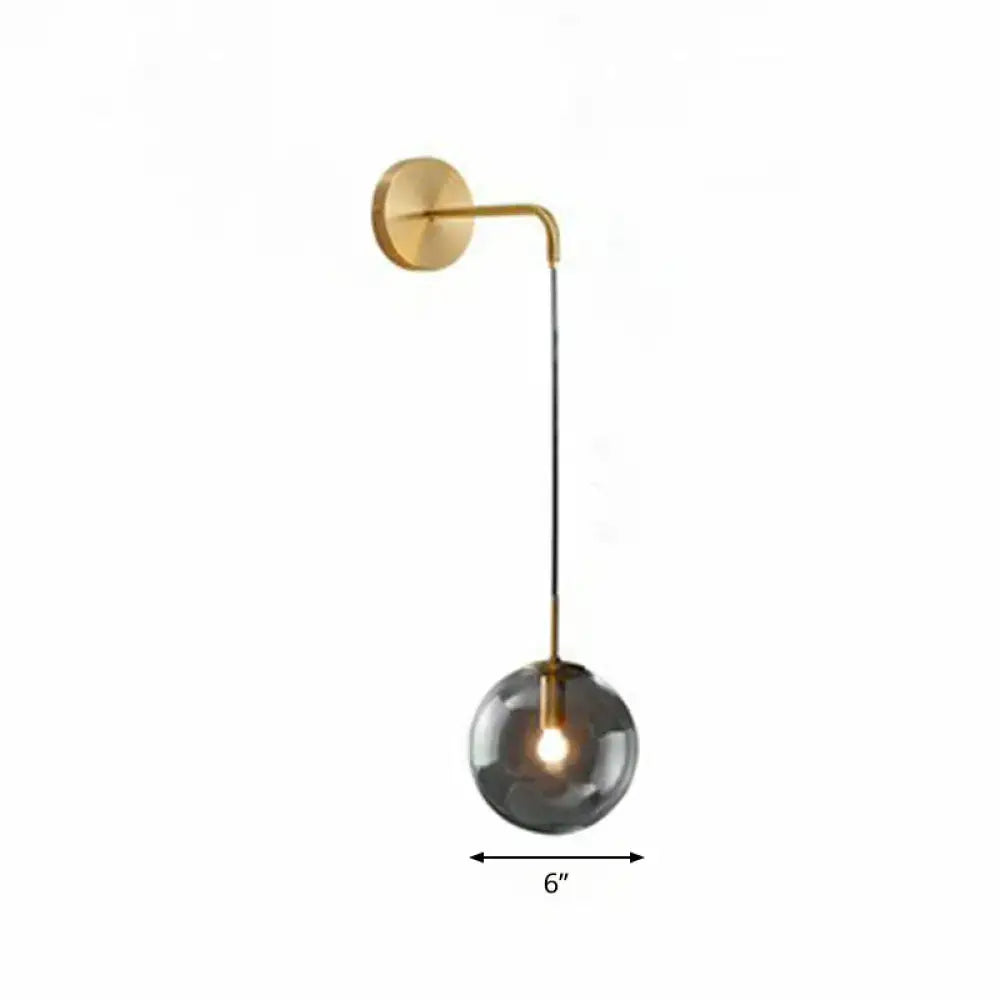 A modern gold and black wall-mounted sconce with a brushed gold finish and spherical smoked glass light bulb