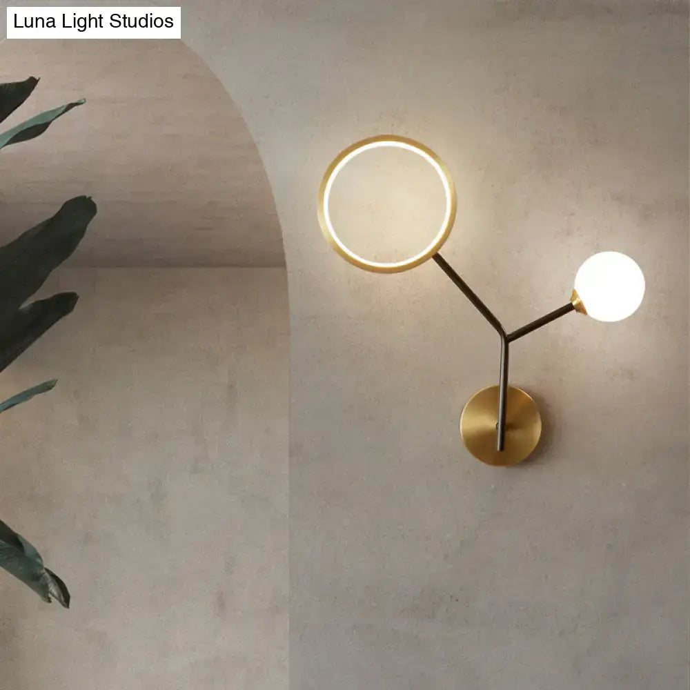 Modern gold and cream glass wall sconce lamp with brass circular ring light and spherical bulb on arched concrete wall