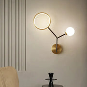 Modern gold and cream glass wall sconce lamp with circular ring light and spherical bulb on sleek brass base for bedroom lighting