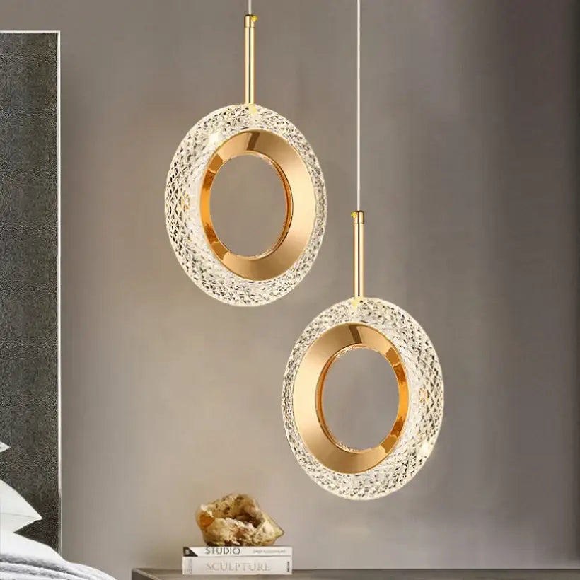 Two elegant gold-toned bedside pendant lights with textured crystal rings and smooth metallic bands for bedroom decor