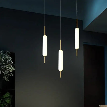 Three modern gold and frosted glass led pendant chandelier lights with cylindrical shades for living room use