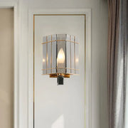 Elegant gold-framed wall sconce with gray glass triangle panels and warm glowing bulb for bedroom lighting