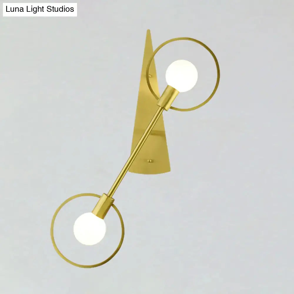 Modern gold-toned double-arm sconce light fixture with circular rings and spherical bulbs for bedroom lighting