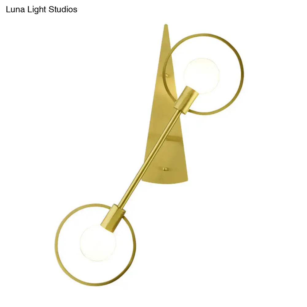 Modern gold-toned sconce light fixture with two circular rings and angular backplate for bedroom lighting
