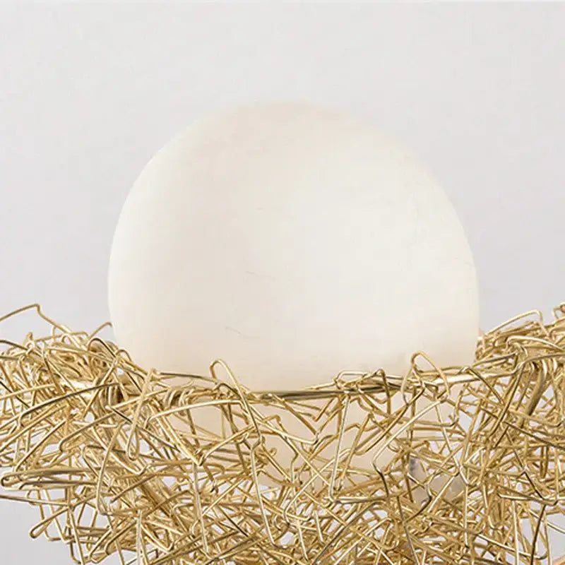 A smooth matte white egg rests in a gold wire nest in modern gold nest glass pendant lights for dining rooms