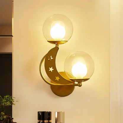 Modern gold wall sconce featuring a gold-toned crescent moon with star cutouts and two spherical glass globes ball wall sconce
