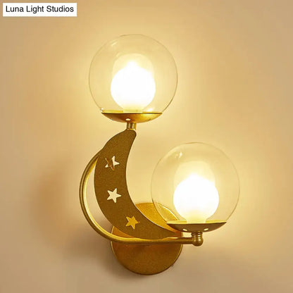 Modern gold-toned crescent moon ball wall sconce with two clear glass globe shades and star cutouts for bedroom lighting