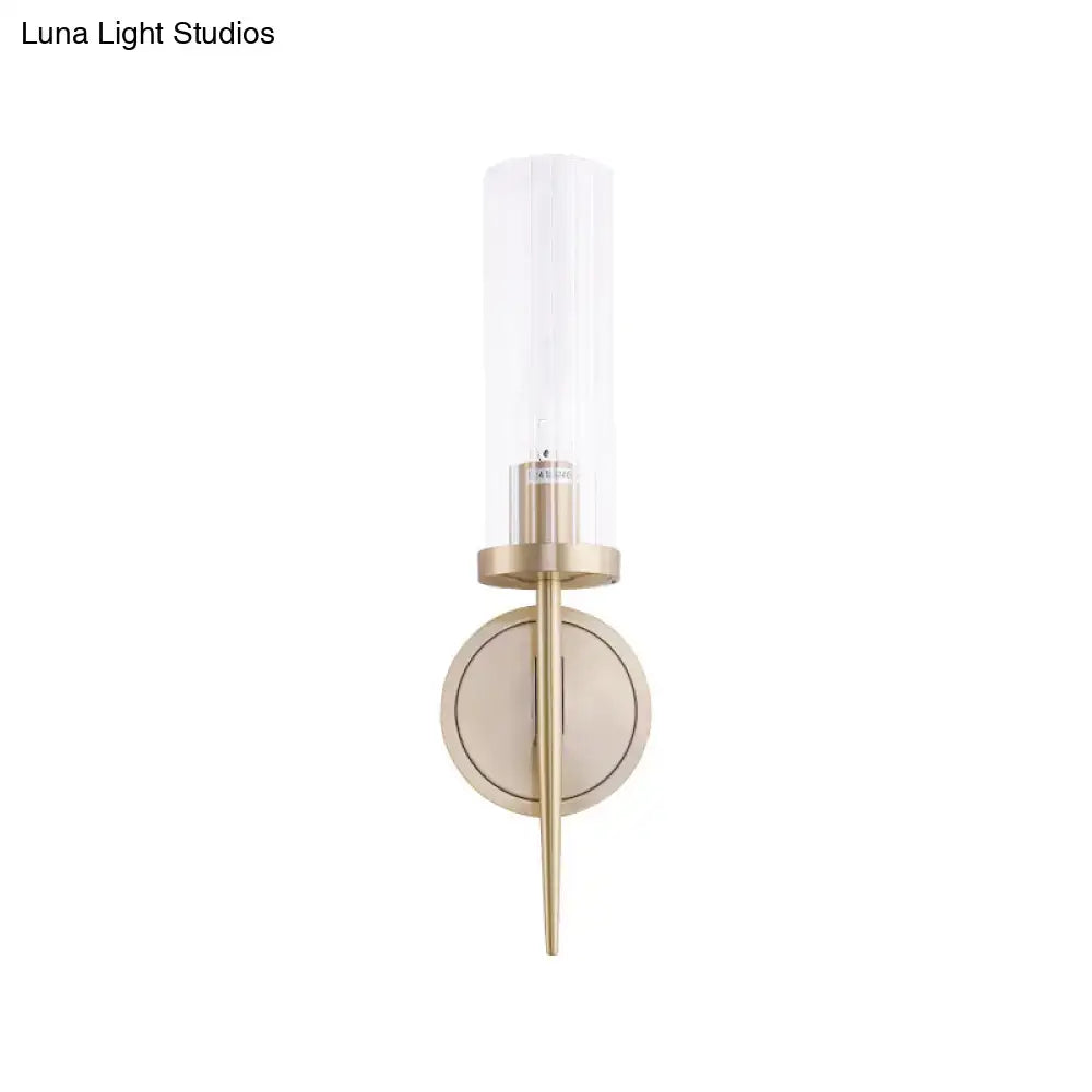 Modern brass-finished wall lamp with clear cylindrical fluted glass shade for bedroom sconce lighting