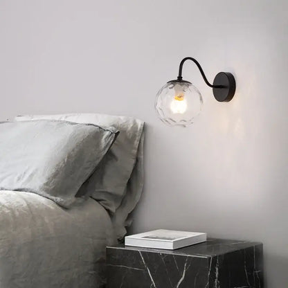 A sleek black wrought iron wall lamp with clear faceted glass globe and illuminated bulb from decorbites glass ballight led