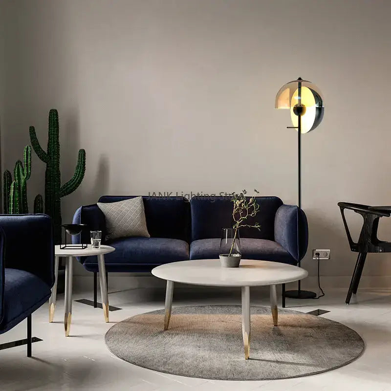 Modern navy blue velvet sofa with textured gray pillow next to sleek modern gold and black decorbites glass hemisphere led floor lamp