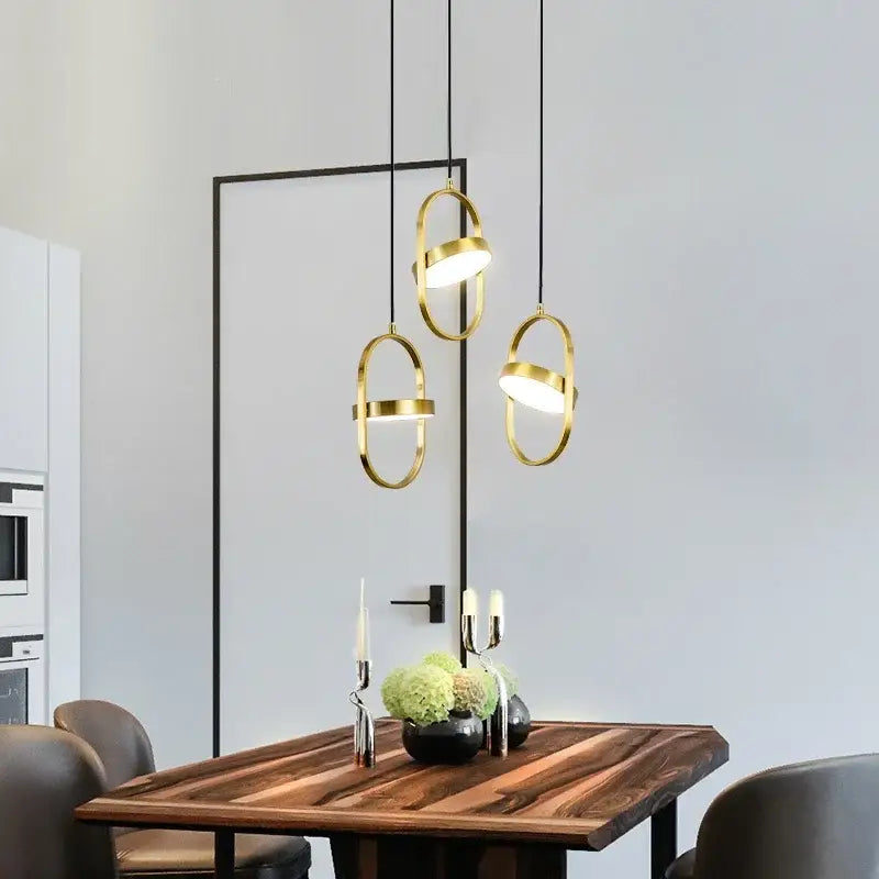 Three modern decorbites gold pendant lights with black cords and oval frames hang above a wooden dining table